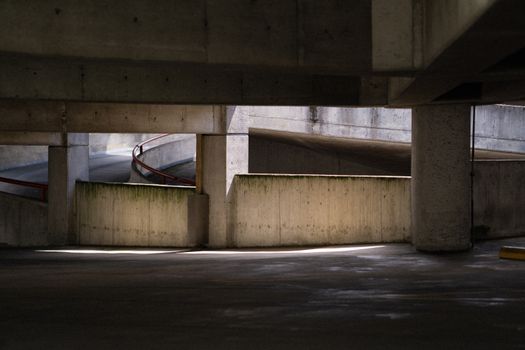 Concrete parking garage with spiral ramp and lighting effects creating shadows.