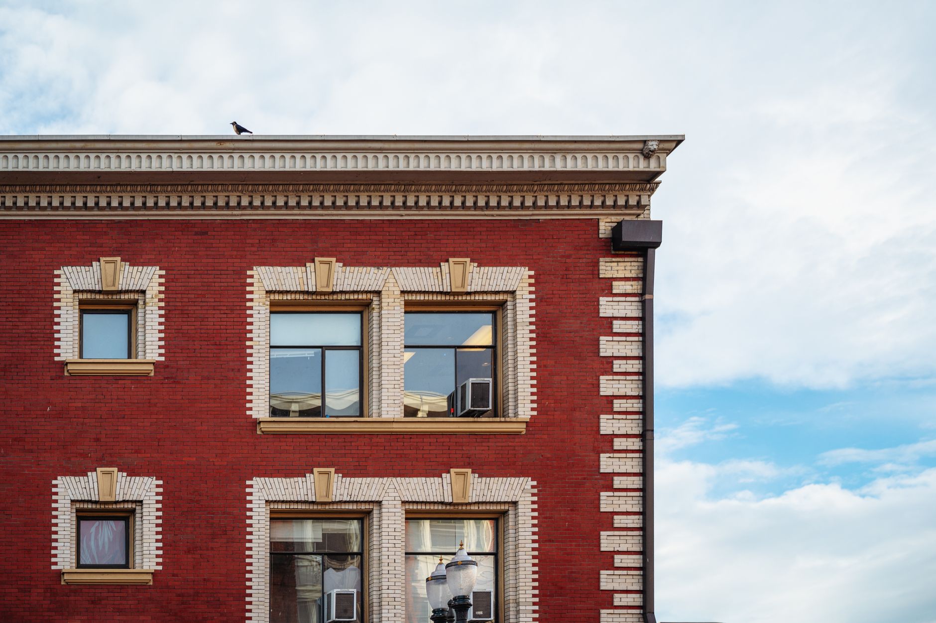 Detailed view of a red brick building facade with windows and a bird perched on the roof corner.