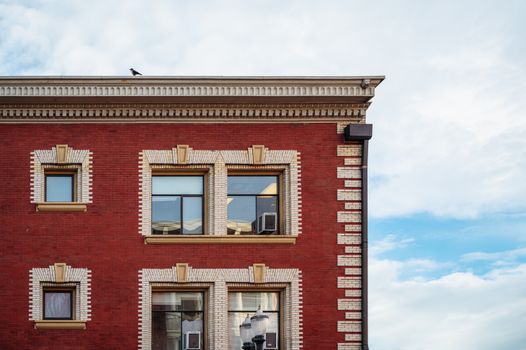 Detailed view of a red brick building facade with windows and a bird perched on the roof corner.