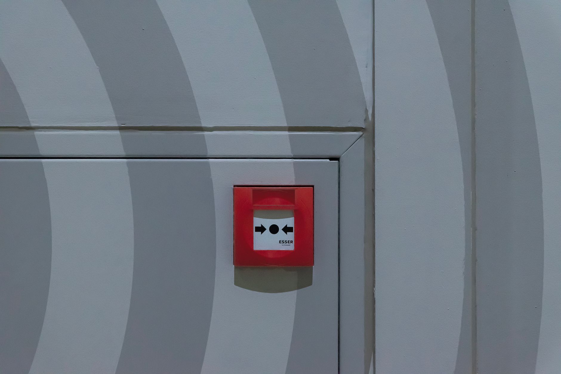 Red emergency button on a grey patterned wall, emphasizing safety measures.