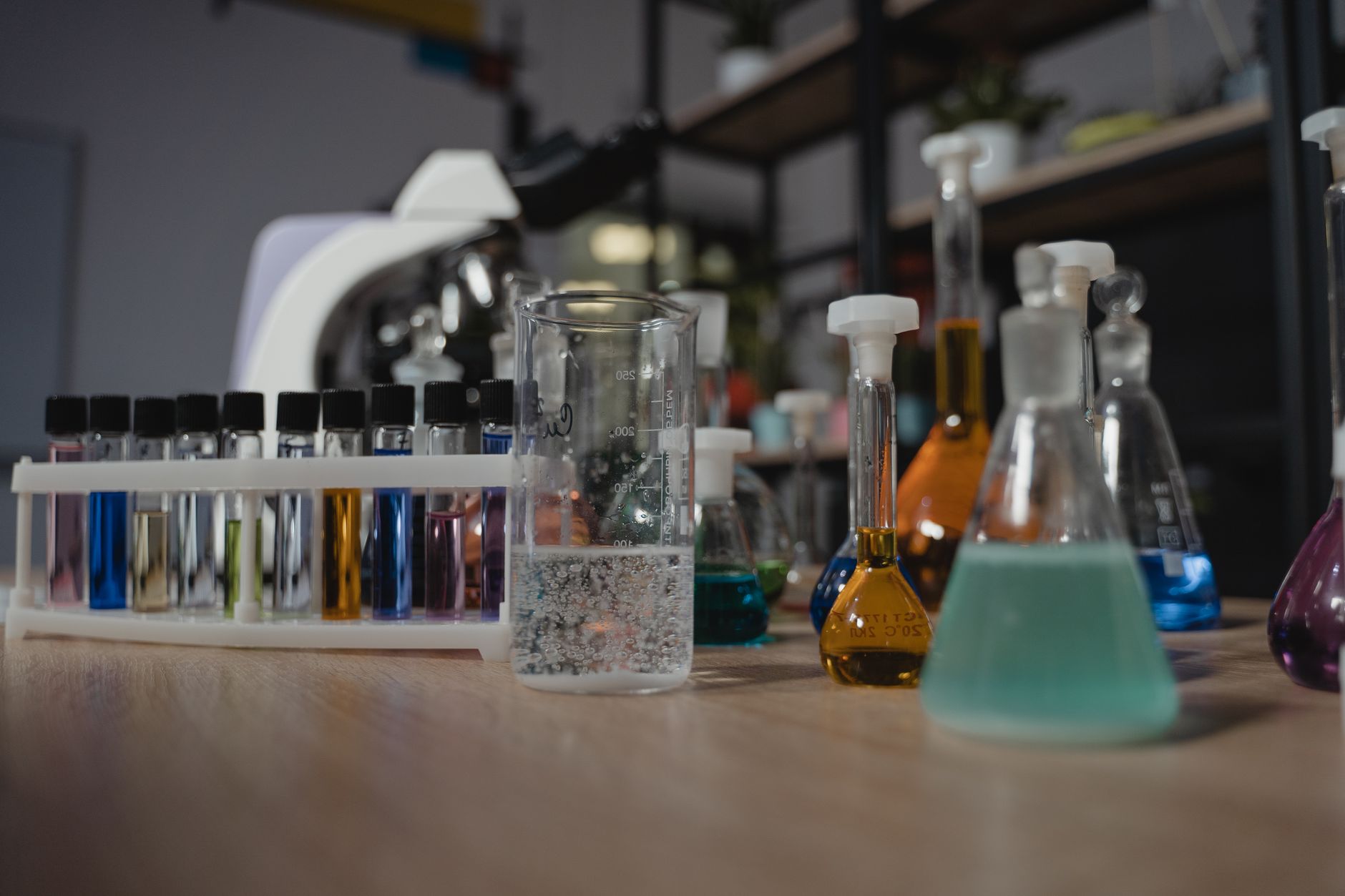 Glassware with colored liquids in a laboratory on a wooden table, showcasing diverse chemical research tools.