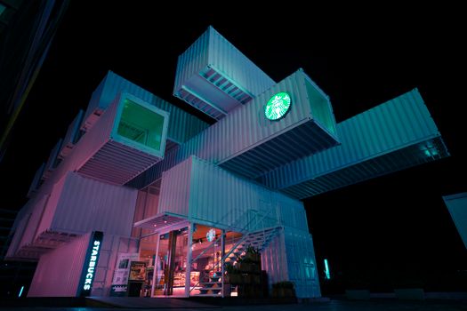 A striking view of a modern Starbucks built from shipping containers, illuminated at night.